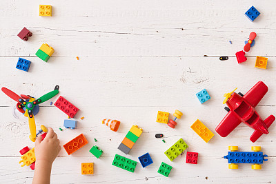 Top view on child's hand playing with multi-color plastic bricks at the table. Toddler having fun and building out of bright constructor bricks. Early learning. Developing toys