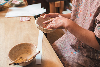 Craftsperson adding strips of paper to a handmade bowl