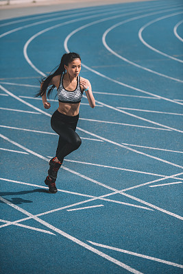 Athletic young sportswoman sprinting on running track stadium