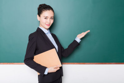 female teacher holding book front of blackboard