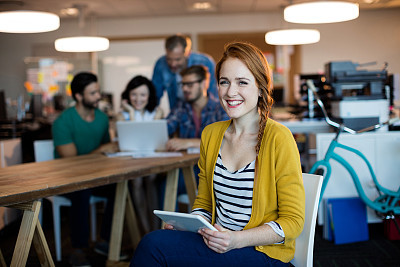 Woman using digital tablet while team working in background