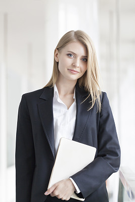 Cheerful young businesswoman standing with digital tablet