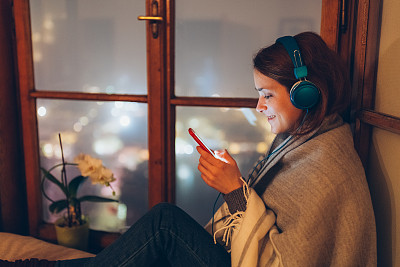 Smiling woman at the window texting on smartphone