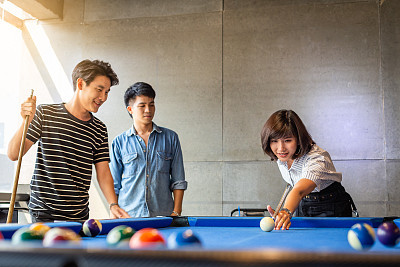 Group of happy friends having fun playing billiard at office together after work