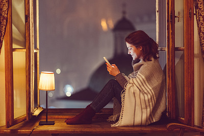Woman sitting on the window sill and texting