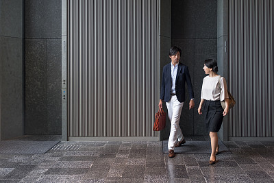 Japanese Businessman and Businesswoman Leaving Office Building Lobby