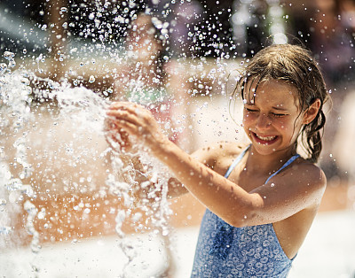 Little girl having fun in water park fountain