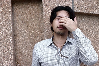 Front view of sad depressed young Asian business man covering face and cry.