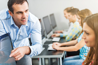 Teacher assisting young woman at computer class.