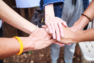 young men and women standing and stacking hands in a meeting on natural ground background at outdoor outing. Teamwork, diversity, collaboration, young generation, harmony, corporate culture concept