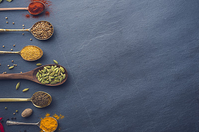 Variety of herbs and spices on slate background.