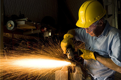 Industry: Man Grinding in workshop wearing hardhat and gloves.  Sparks