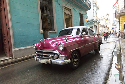 Pink colored retro vehicule driving on streets in Cuba