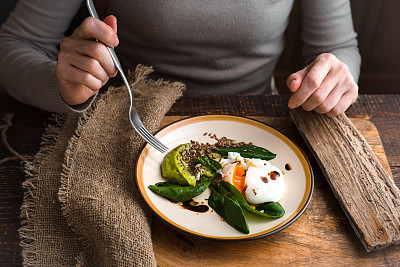 Woman eating poached egg with avocado cream horizontal