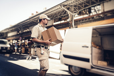 Messenger delivering parcel, walking in street next to his van