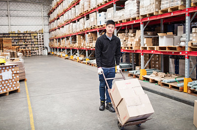 Worker pushing trolley with boxes in warehouse