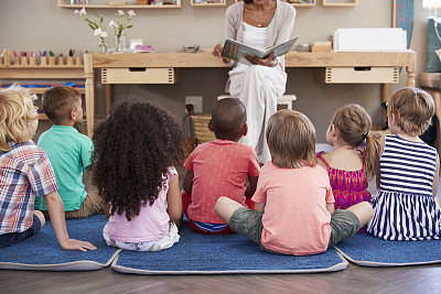 Teacher At Montessori School Reading To Children At Story Time