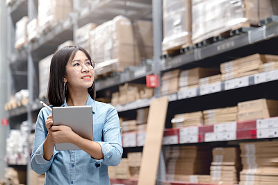 Young attractive asian worker, owner, entrepreneur woman holding smart tablet computer looking side up above shelf with efulfillment service business warehouse online concept. Asian sme merchandise.