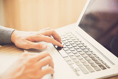 Close-up of male hands typing on laptop indoors