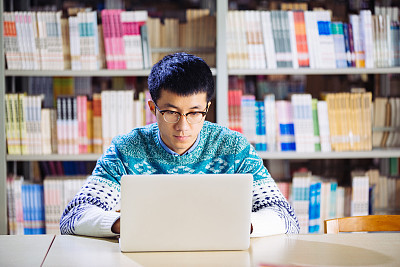 young asian man with laptop in library