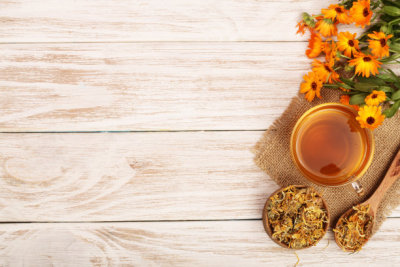 Calendula tea with fresh and dried flowers on white wooden background with copy space for your text. Top view