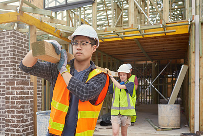 Builders carrying a wood beam at construction site