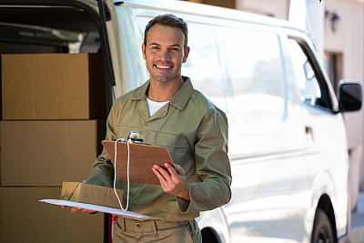 Happy delivery man holding cardboard box and clipboard