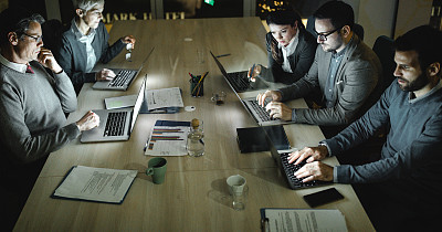 Panoramic view of group of entrepreneurs working on laptops late in the office.