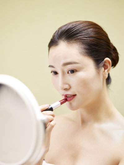 young asian woman looking at mirror while applying lipstick