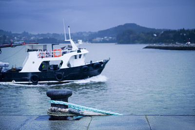 Harbor mooring post, thick ropes, fishing boat, seascape background.