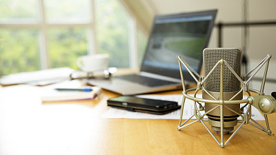 workspace for journalism with condenser microphone, laptop, cellphone and notepad on a desktop at the window, short panoramic banner for website headerwith blurred background, copy space