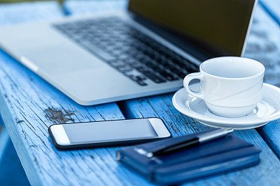 Opened laptop with smartphone, pen and cup of coffee