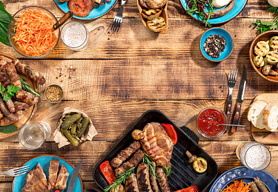 Appetizing barbecued steak, sausages and grilled vegetables on a wooden picnic table with copy space