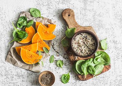 Raw ingredients for cooking vegetarian lunch - pumpkin, wild rice, spinach, spices on a light table, top view. Flat lay