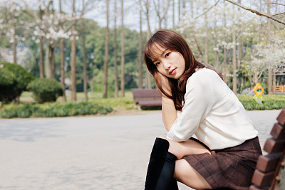 Outdoor portrait of beautiful young Chinese girl smiling among blossom cherry tree brunch in spring garden, beauty, summer, emotion, expression and people lifestyle concept.