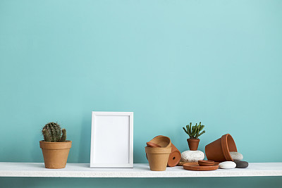 Modern room decoration with picture frame mockup. White shelf against pastel turquoise wall with pottery and succulent plant with potted cactus.