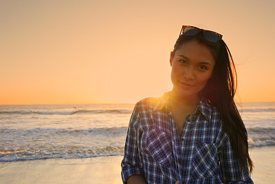 Beautiful young Asian woman standing on beach at sunset