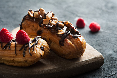 Eclairs with peanuts, chocolate icing and raspberries