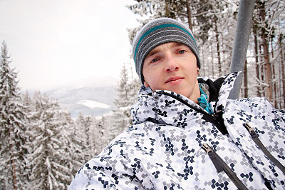 Happy man rises on the lift in Carpathian mountains. On background of forest and ski slopes. Close up. Winter nature. Heavy snow falls.