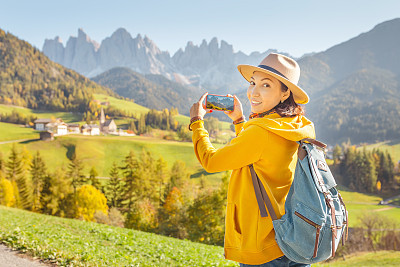 Woman traveler making photo with her smartphone in Funes Valley, Dolomites Alps in Italy