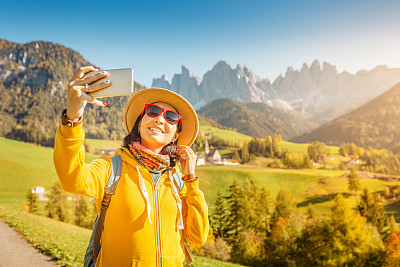 Woman traveler making photo with her smartphone in Funes Valley, Dolomites Alps in Italy