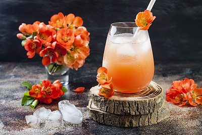 Floral pastel peach and pink brunch cocktail garnished with quince flowers over old rustic background.