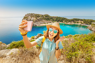 Asian Girl in a hat takes a selfie on the background of stunning views of the azure Bay in the Mediterranean sea. Travel, vacation and mobile connection concept