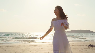 Young Asian woman walking on beach. Beautiful female happy relax walking on beach near sea when sunset in evening. Lifestyle women travel on beach concept.