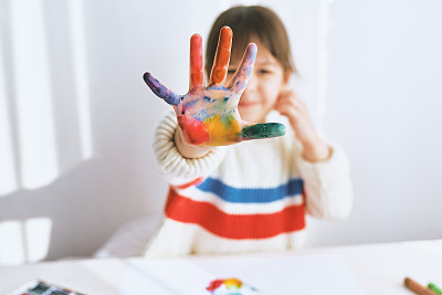 Closeup portait of happy little girl smiling and showing her colorful hand. Pretty creative child painting and learning colors at kindergarten. People, childhood, education