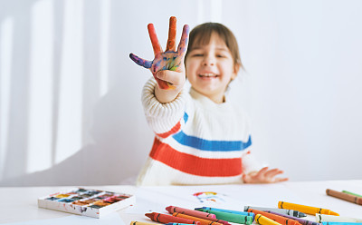 Horizontal portrait of happy little girl smiling and showing her colorful fingers. Pretty creative child painting and learning colors at kindergarten. People, childhood, education