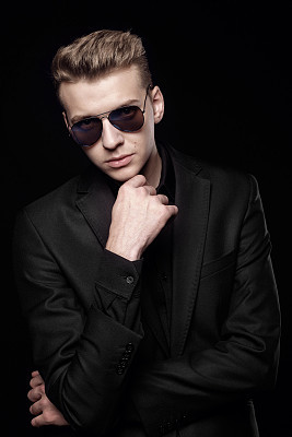 young man with black glasses in black jacket on black background