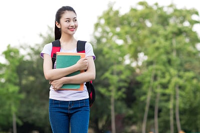 female student outdoors holding a notebook and smiling