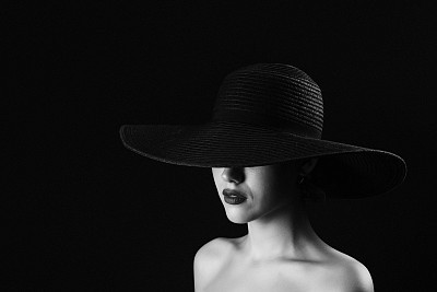 Monochrome studio shot of young beautiful woman wearing hat