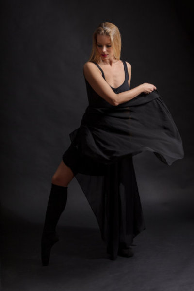Female ballet dancer dancing in black dress against black background